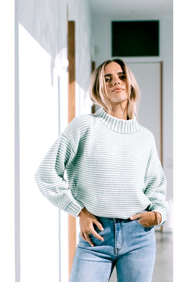 Woman wearing a Billie Stitch Stripe Knit in sage and blue jeans standing front on indoors.