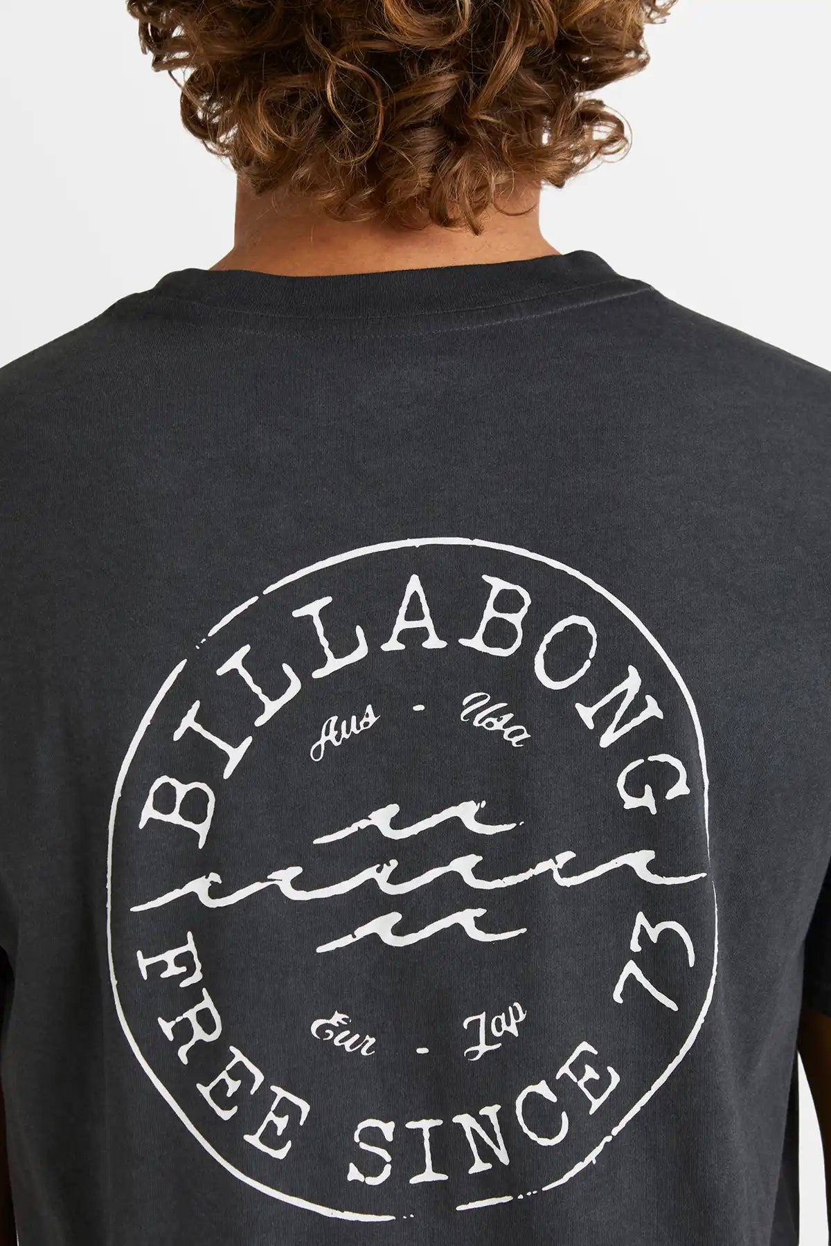 Black t-shirt with Billabong logo on the back, worn by a person.