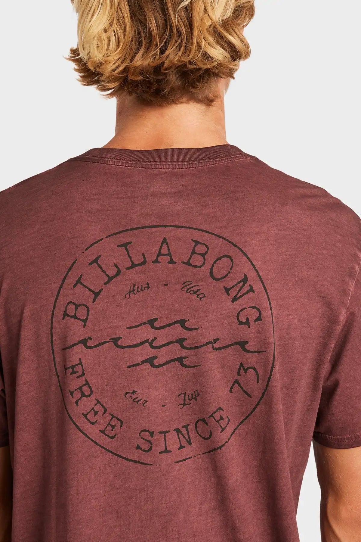 Person wearing a maroon Billabong t-shirt with branding on the back