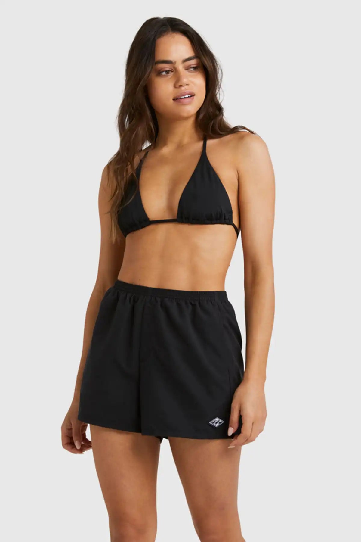 Woman wearing a black bikini with Billabong Womens Sandbar Boardshorts on plain background