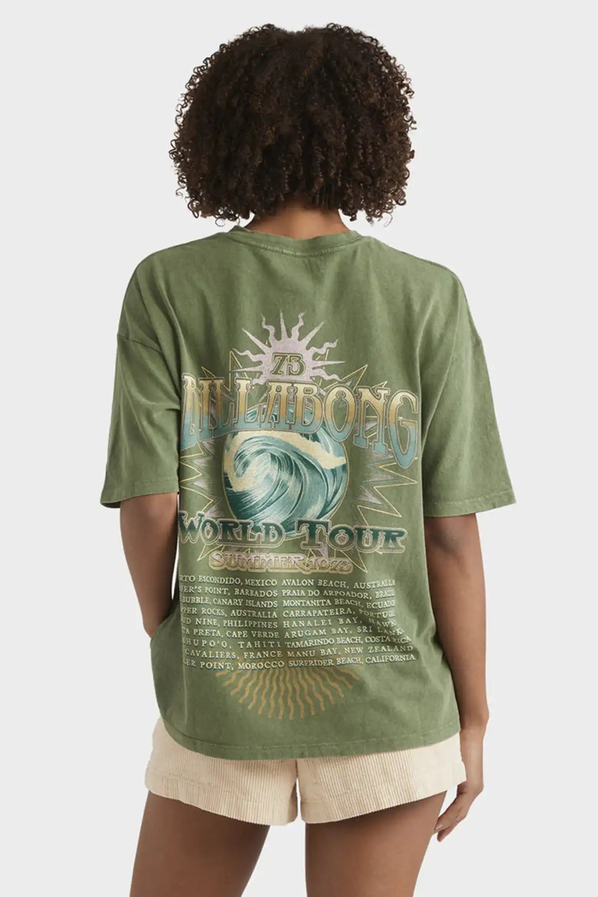 Person wearing a Billabong Women's Take A Tour Tee in Luv Army with a graphic design on the back, standing against a plain background