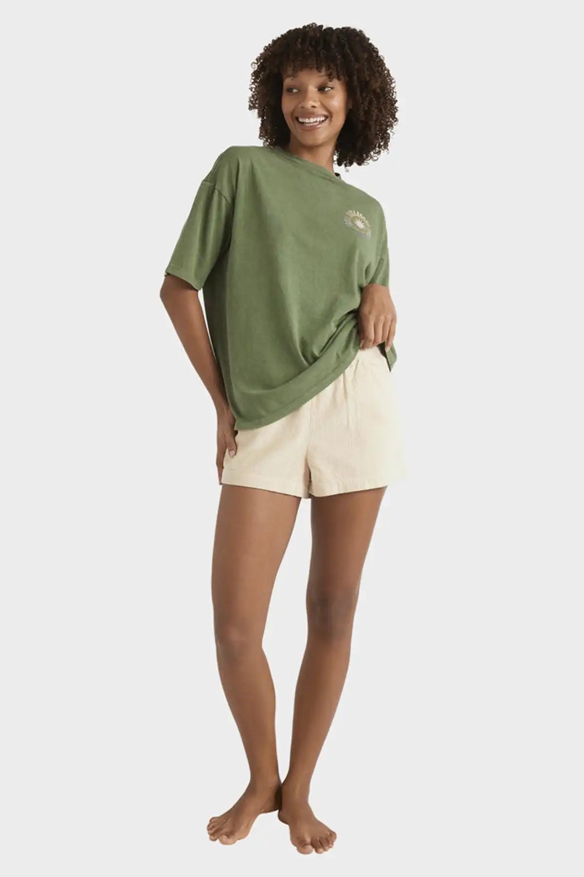 Woman wearing a Billabong Women's Take A Tour Tee in Luv Army and beige shorts on a white background