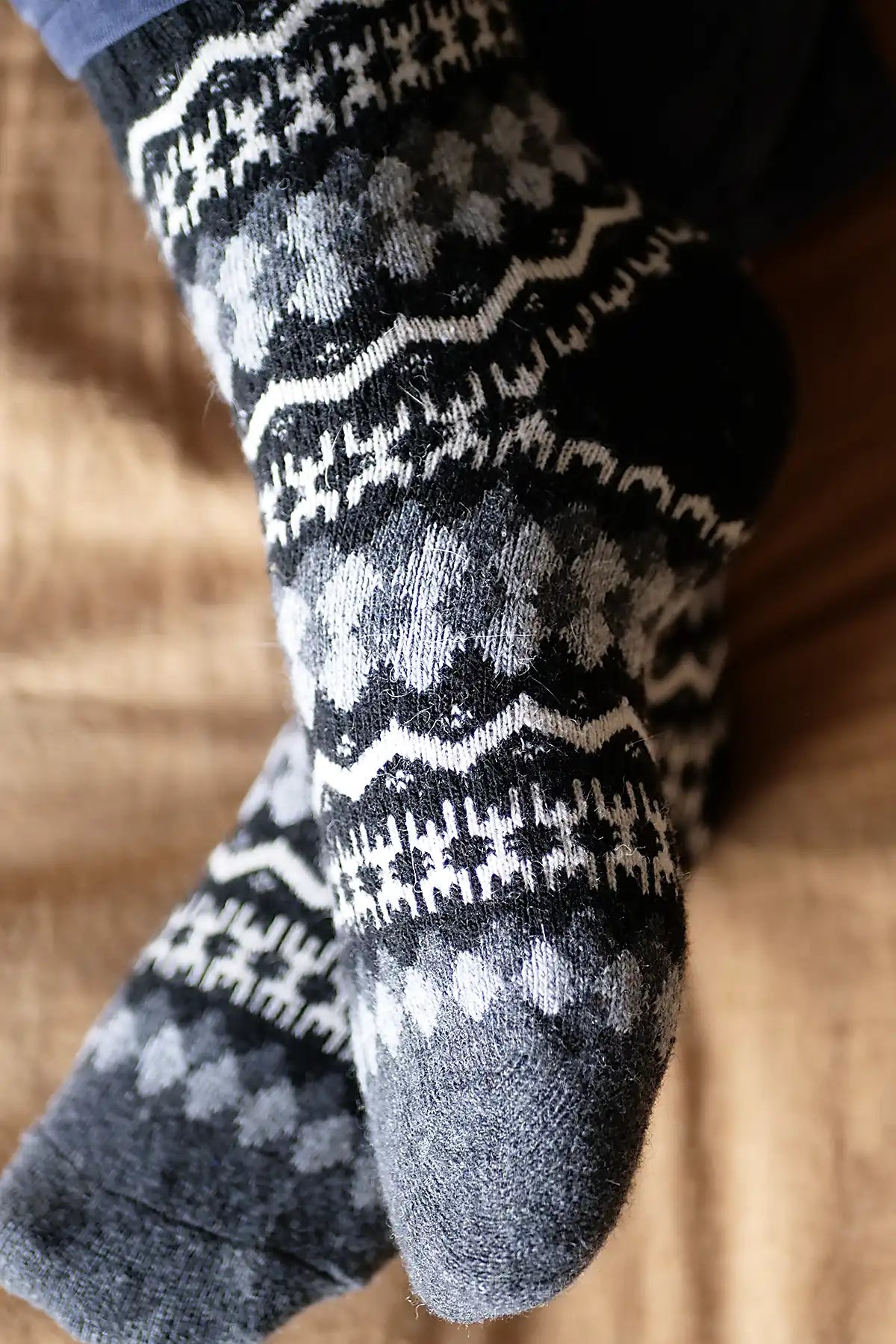 Close-up of feet wearing black and gray patterned socks on a wooden floor.