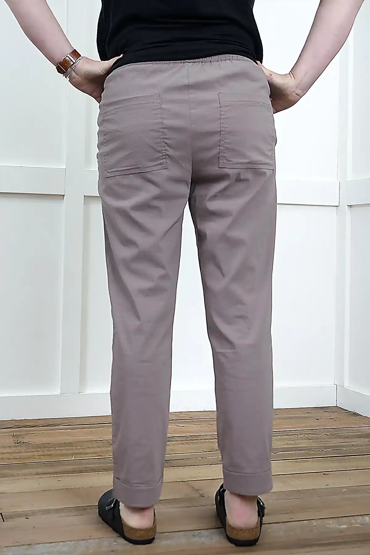 Person wearing Clara Cotton Blend Pull-On Pants in Mushroom standing back on against a wooden floor with a white wall background