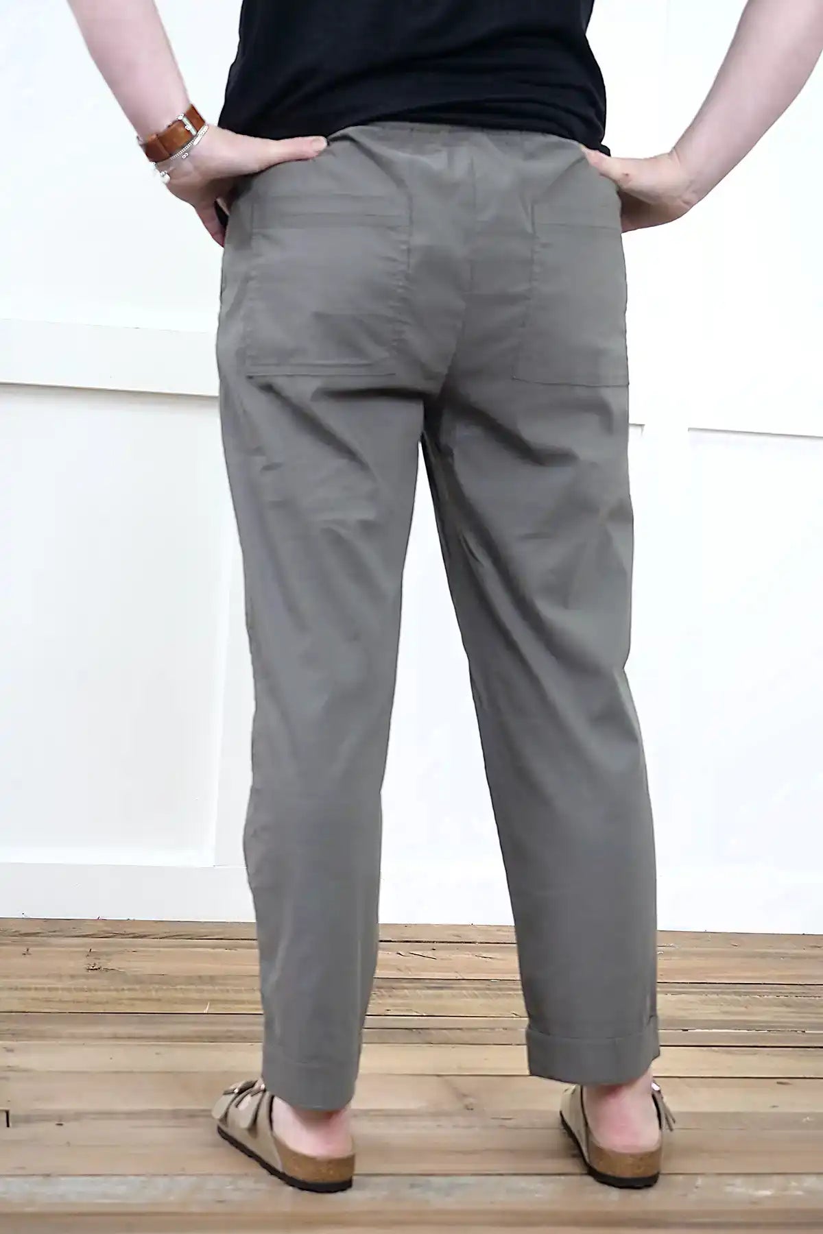Person wearing Clara Cotton Blend Pull-On Pants in Olive standing back on with wooden floor with a white wall background