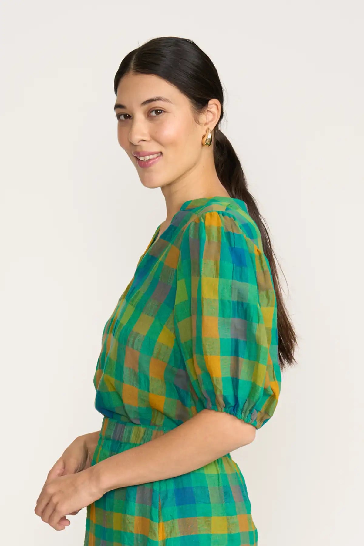Woman wearing a Foil Checkmate Top – Green Check on a white background side view