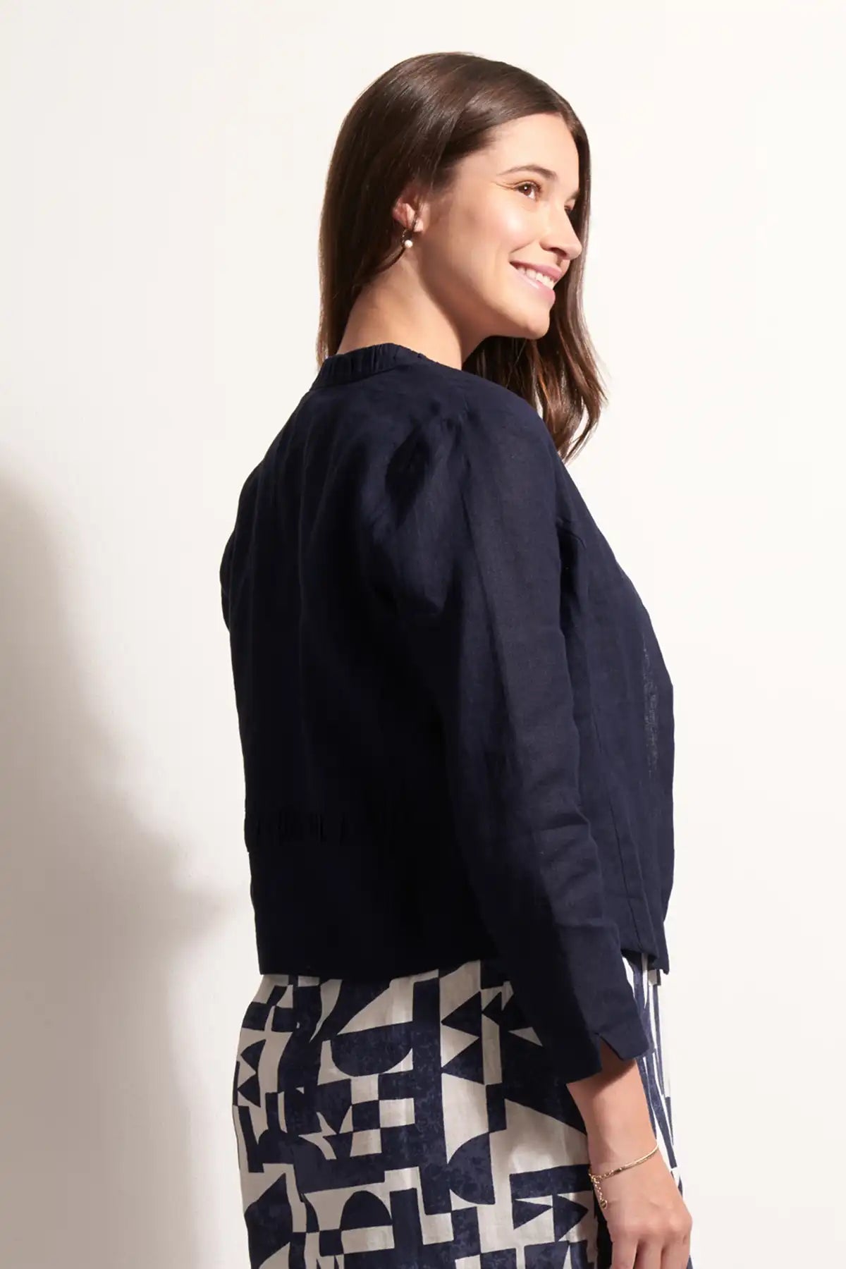 Woman wearing a x Foil Linen Gather Together Jacket in True Navy and patterned skirt on a white background back view