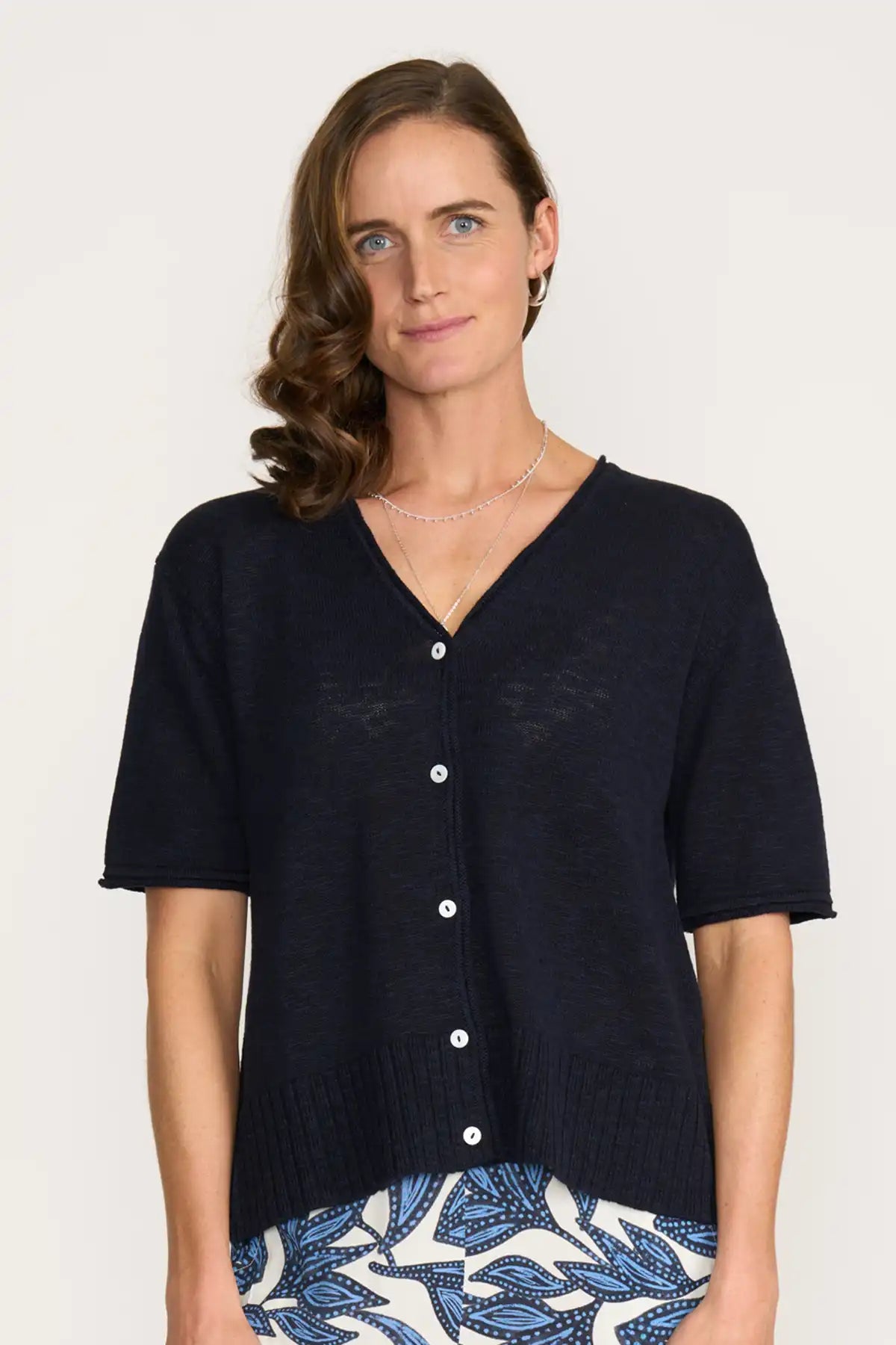 Woman wearing a Foil Nitty Gritty Cardigan in True Navy over a patterned skirt on a white background front detailed view