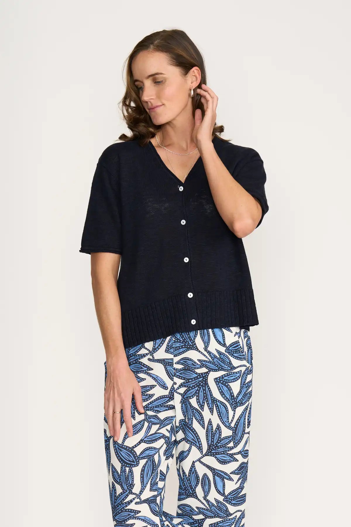 Woman wearing a Foil Nitty Gritty Cardigan in True Navy over a blue and white patterned skirt on a white background front view