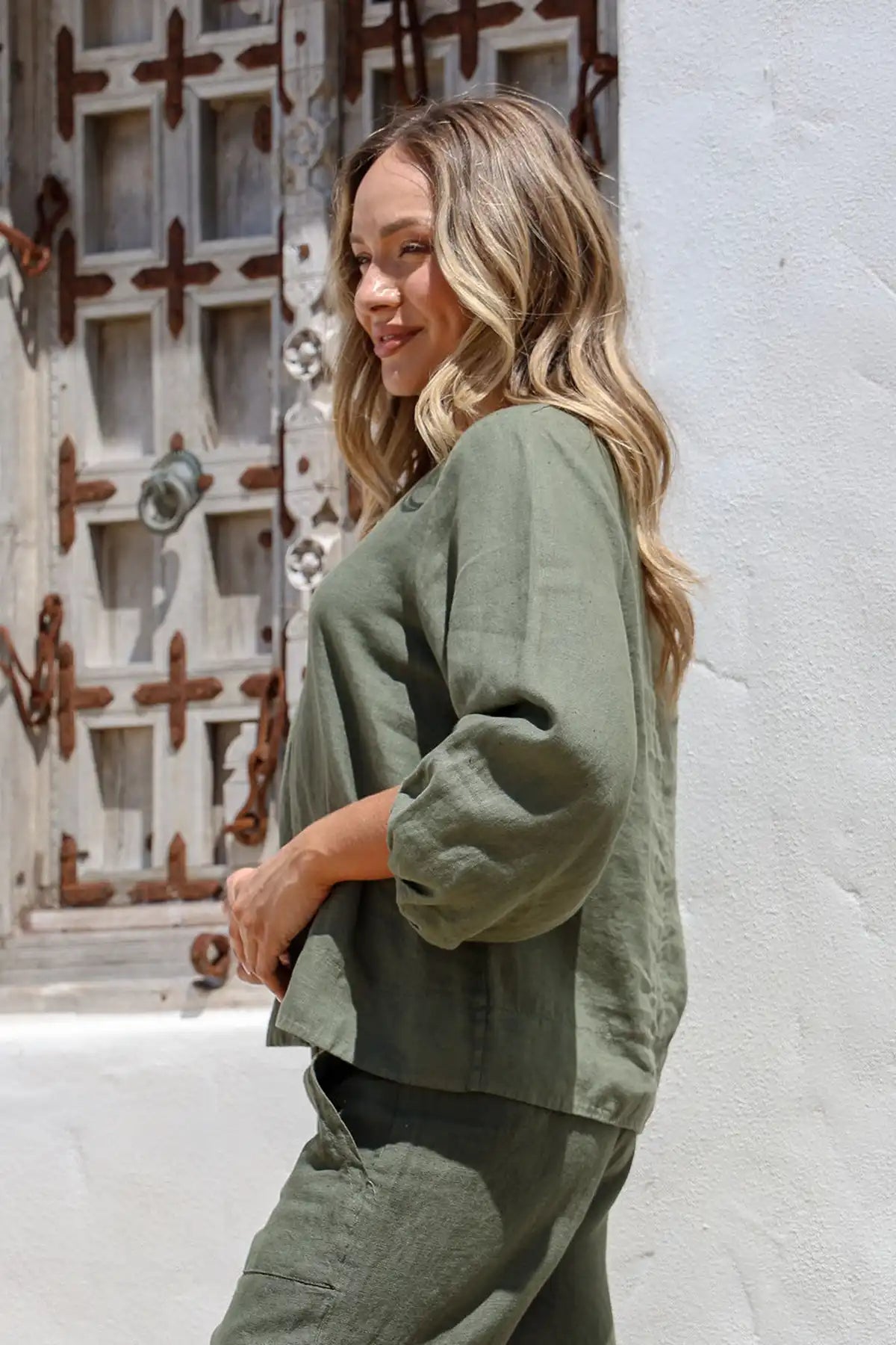 Woman wearing a Giovanna Italian Linen Top in Juniper standing side on against a textured wall.