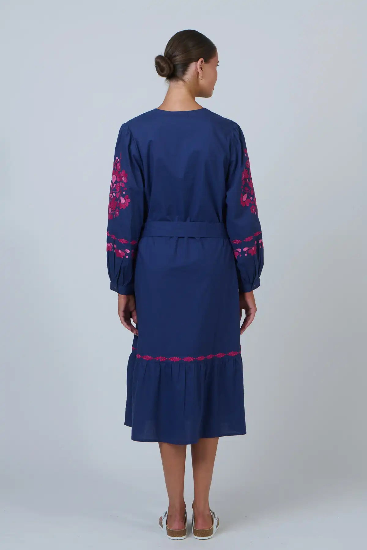 woman wearing Ink Rose Embroidered Midi Dress and white sandals staning back on against a white background