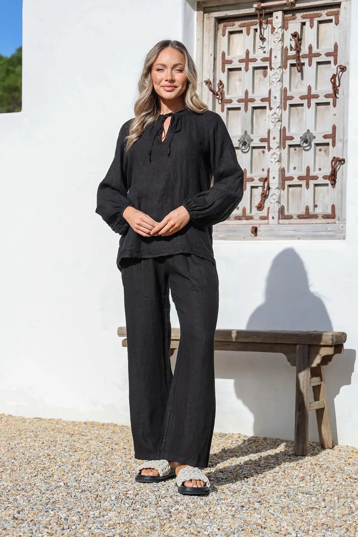 Woman in black outfit with Italian Linen Pant in Black, standing in front of a white wall with a decorative door.