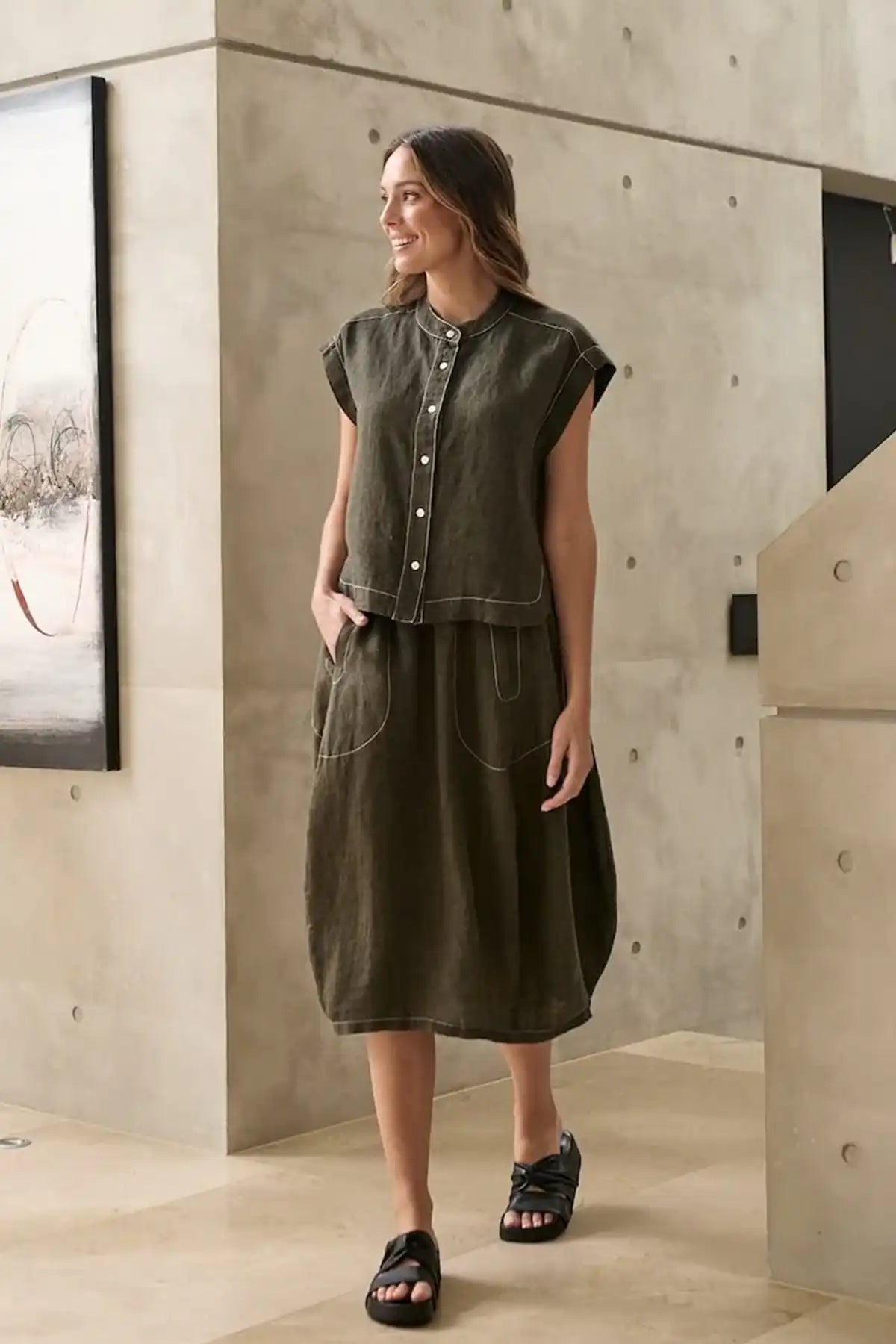 Woman wearing an Licorice Linen Skirt and top standing in a modern indoor setting.