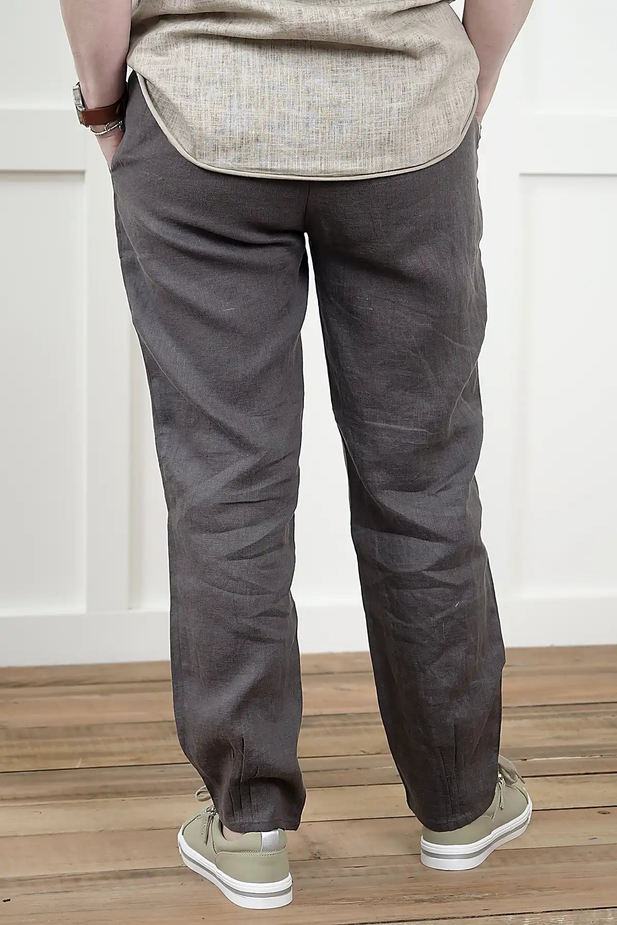 Person wearing Lina Linen Pull-On Pants in Charcoal from behind and a light shirt standing on a wooden floor with a white wall background