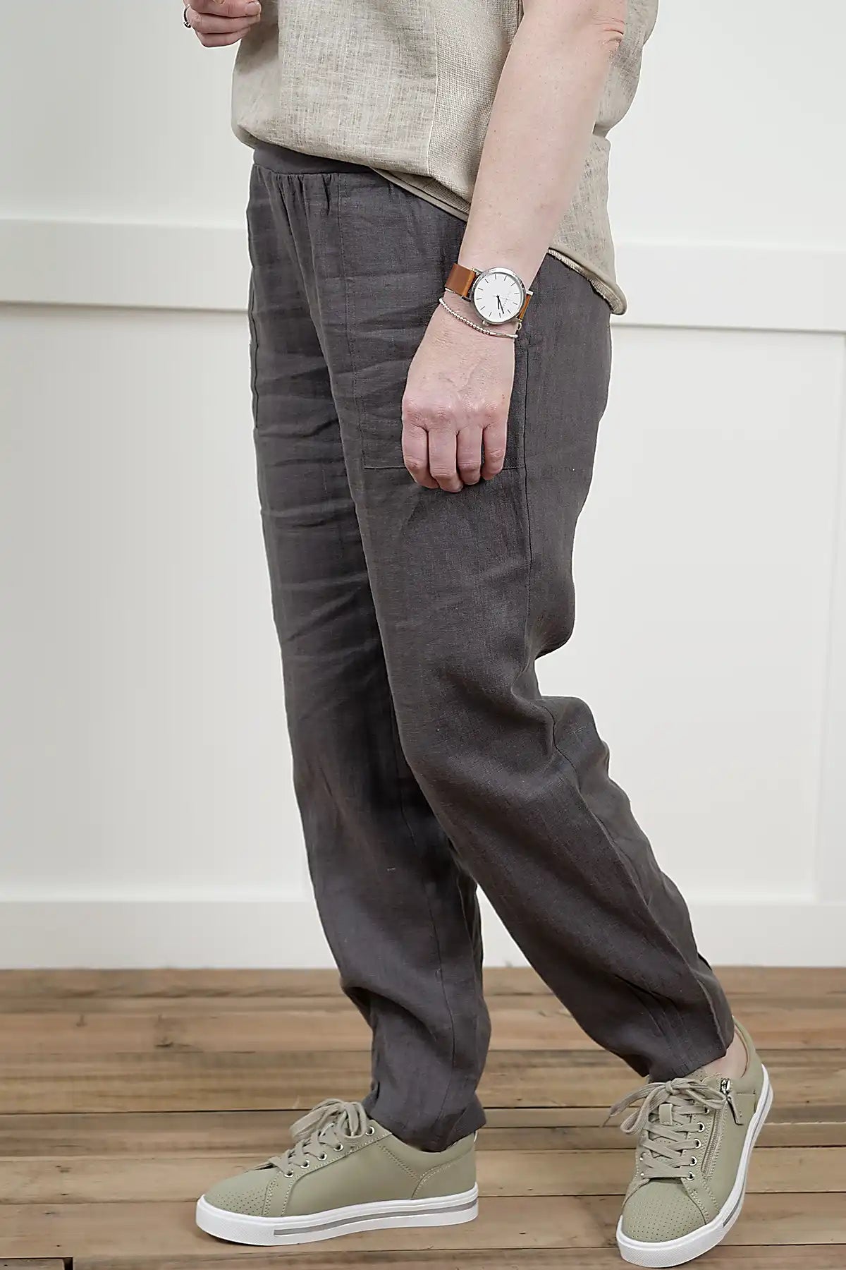 Person wearing Lina Linen Pull-On Pants in Charcoal side view and beige shoes on a wooden floor.