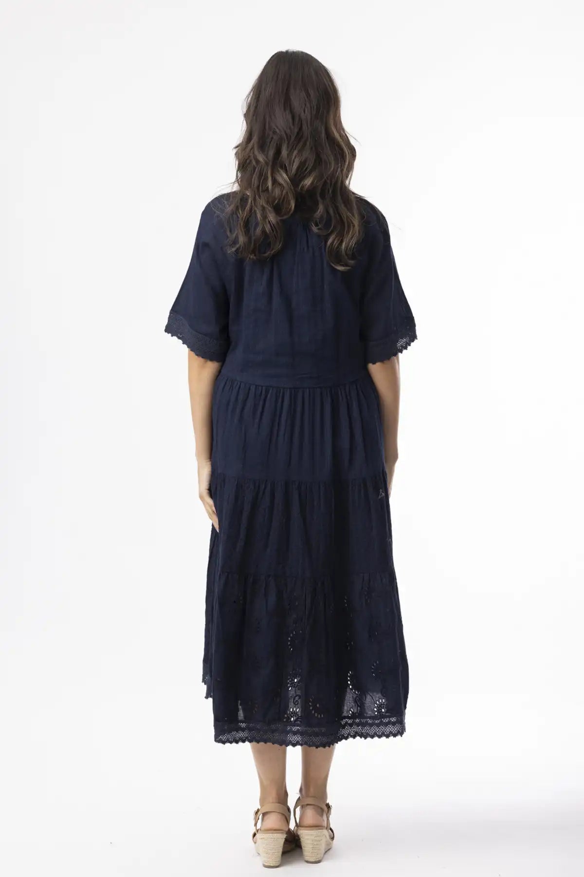 Woman wearing a navy blue dress with lace details on a white background back to camera