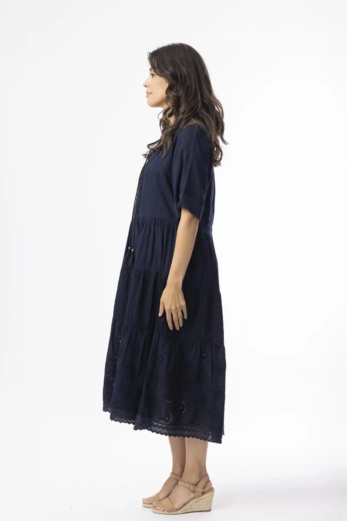 Woman wearing a dark blue dress on a white background standing side on to camera