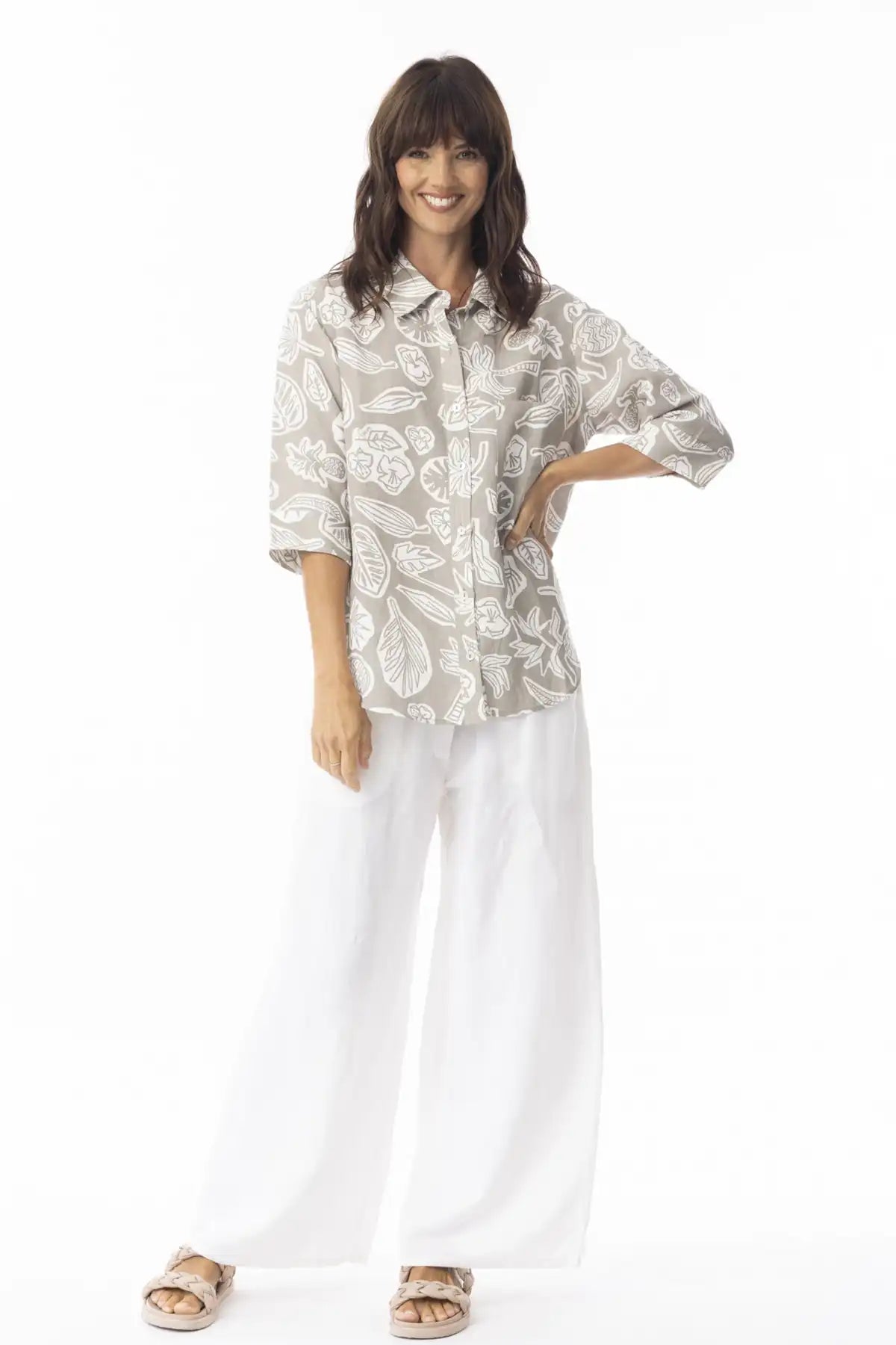 Woman wearing a Orientique Escape Linen Boxy Collar Shirt in sand print and white pants on a white background
