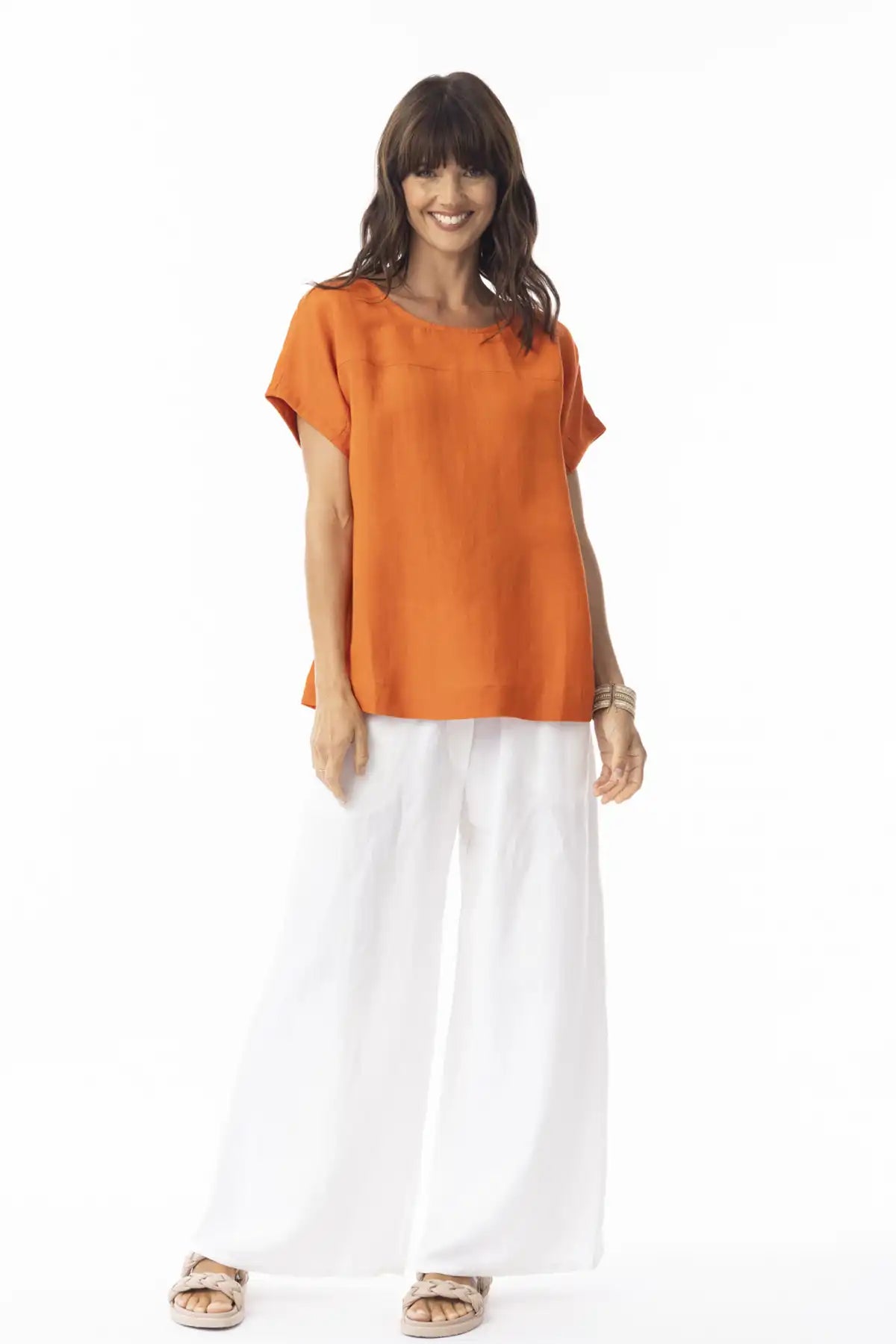 Woman wearing an Orientique Escape Linen Solid Boxy Top in Mandarin and white pants on a white background