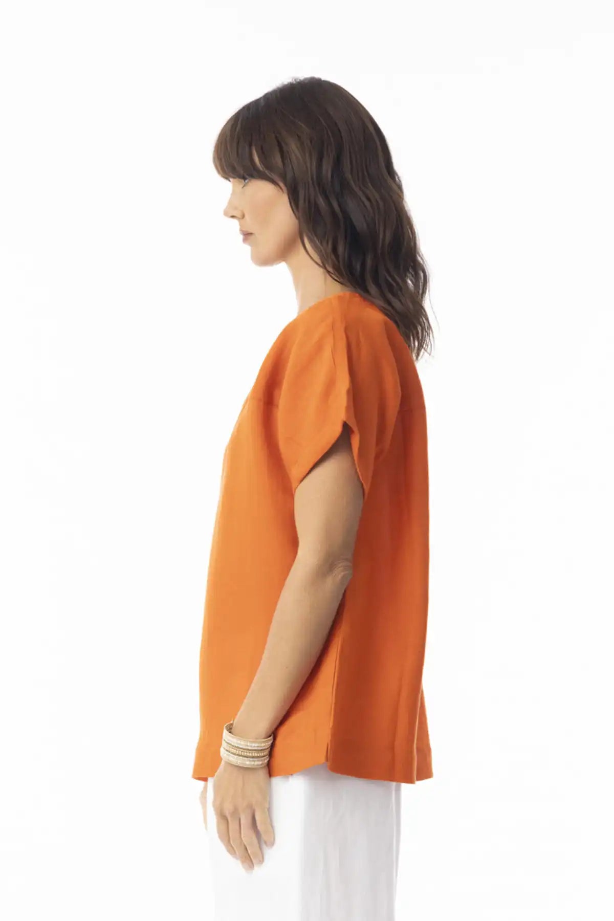 Woman wearing an Orientique Escape Linen Solid Boxy Top in Mandarin and white pants on a white background side view