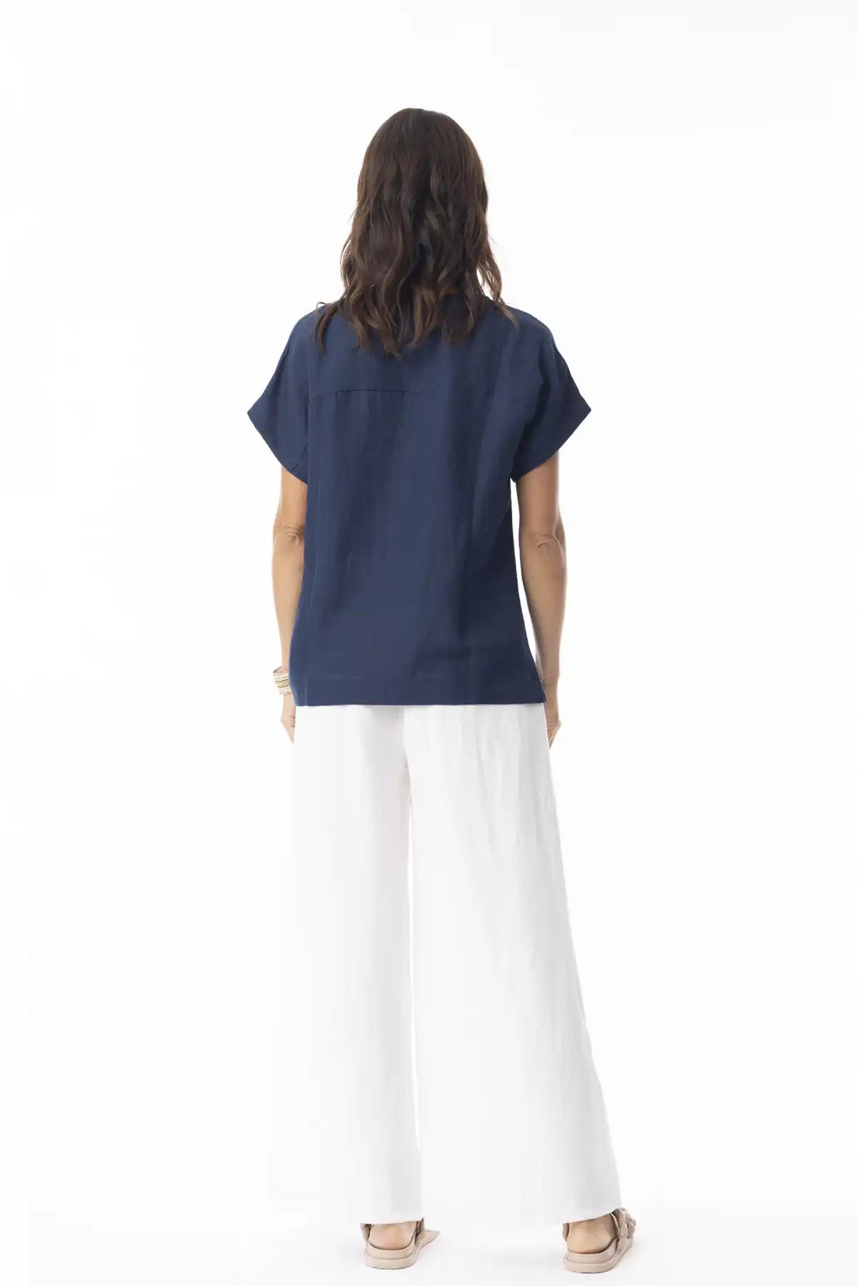 Person wearing a Orientique Escape Linen Solid Boxy Navy Top and white pants on a white background back view