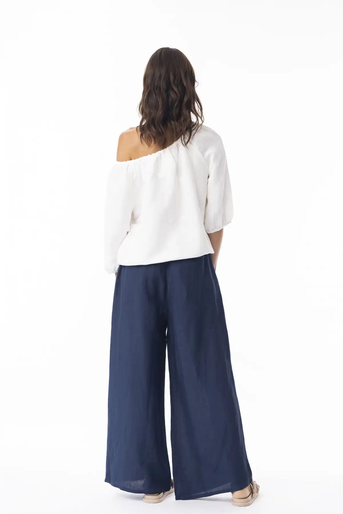 Woman wearing a white top and Orientique Escape Linen Wide Leg Navy Pants from behind on a white background