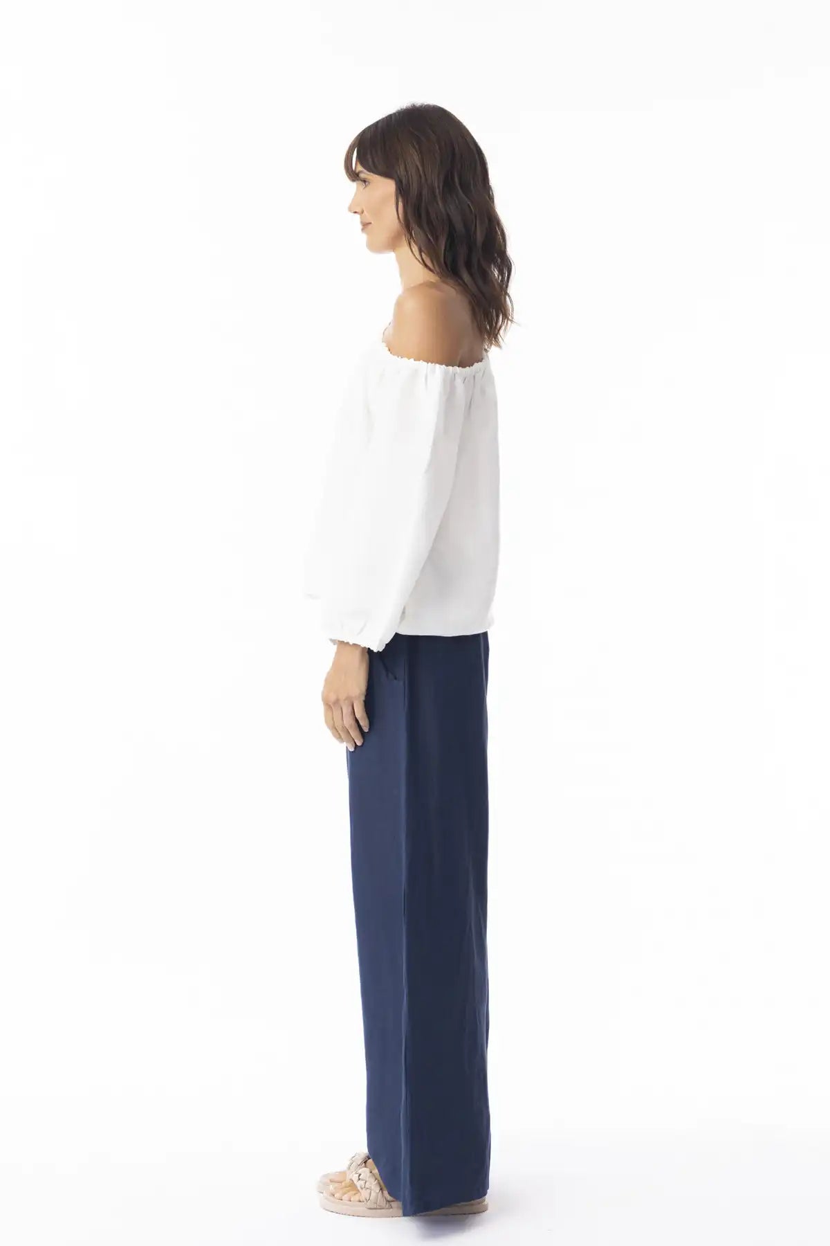 Woman wearing a white off-shoulder top and Orientique Escape Linen Wide Leg Navy Pants on a white background side view