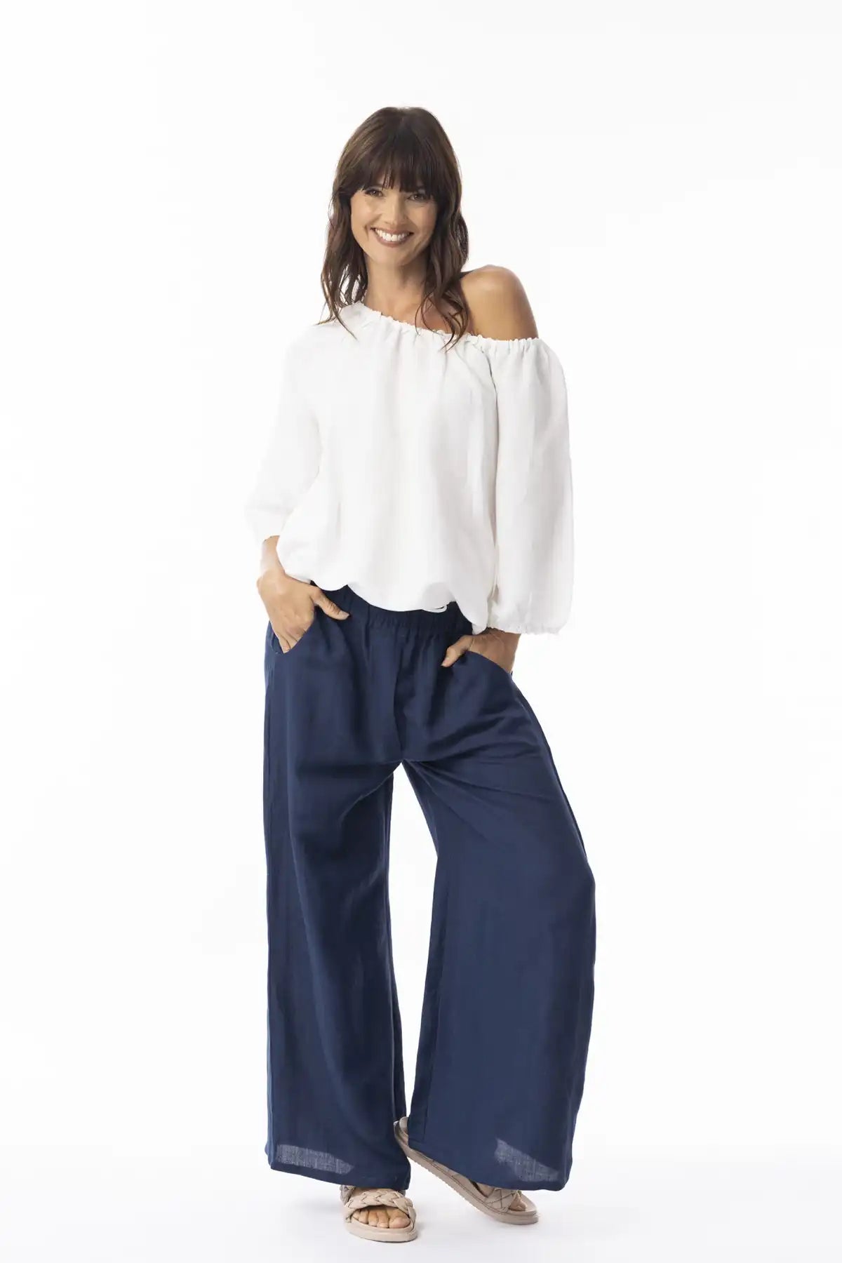 Woman wearing a white off-shoulder top and Orientique Escape Linen Wide Leg Navy Pants on a white background