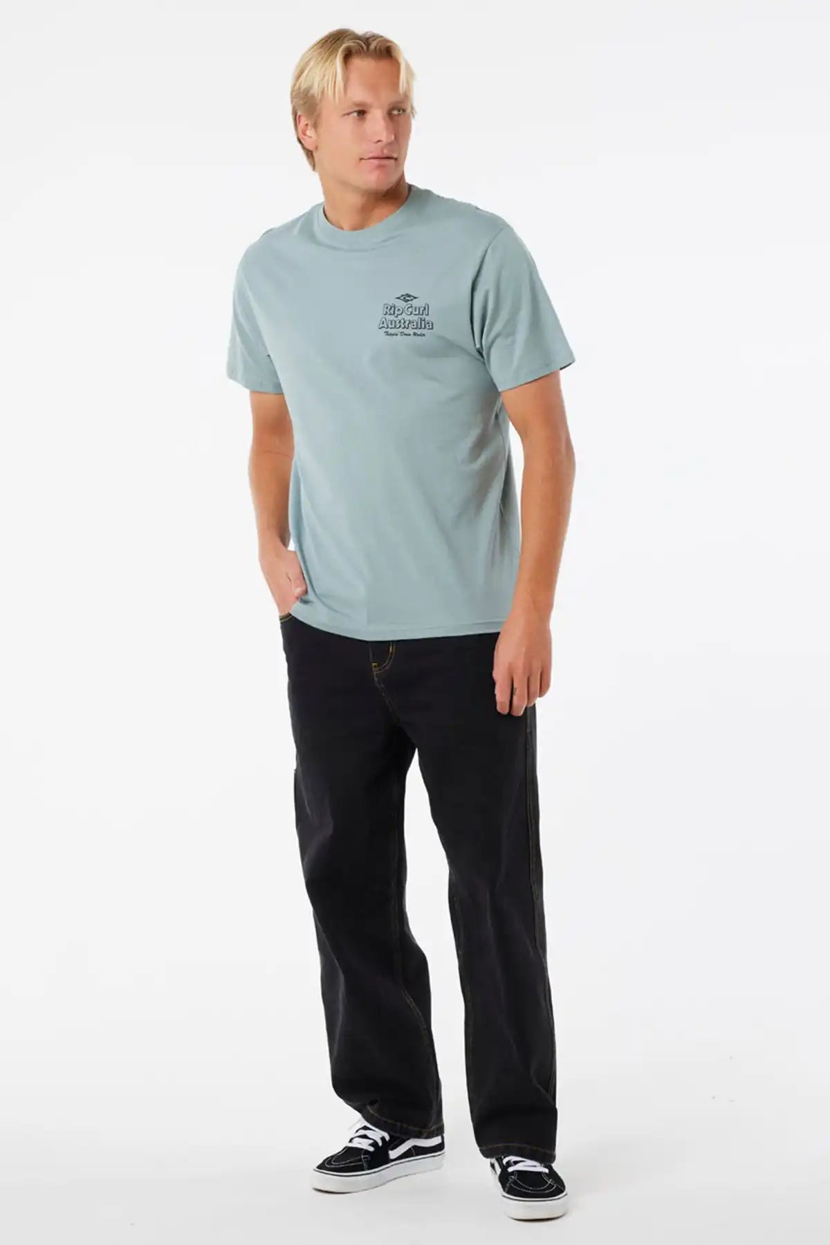 Man wearing a light blue t-shirt with a logo and black pants on a white background