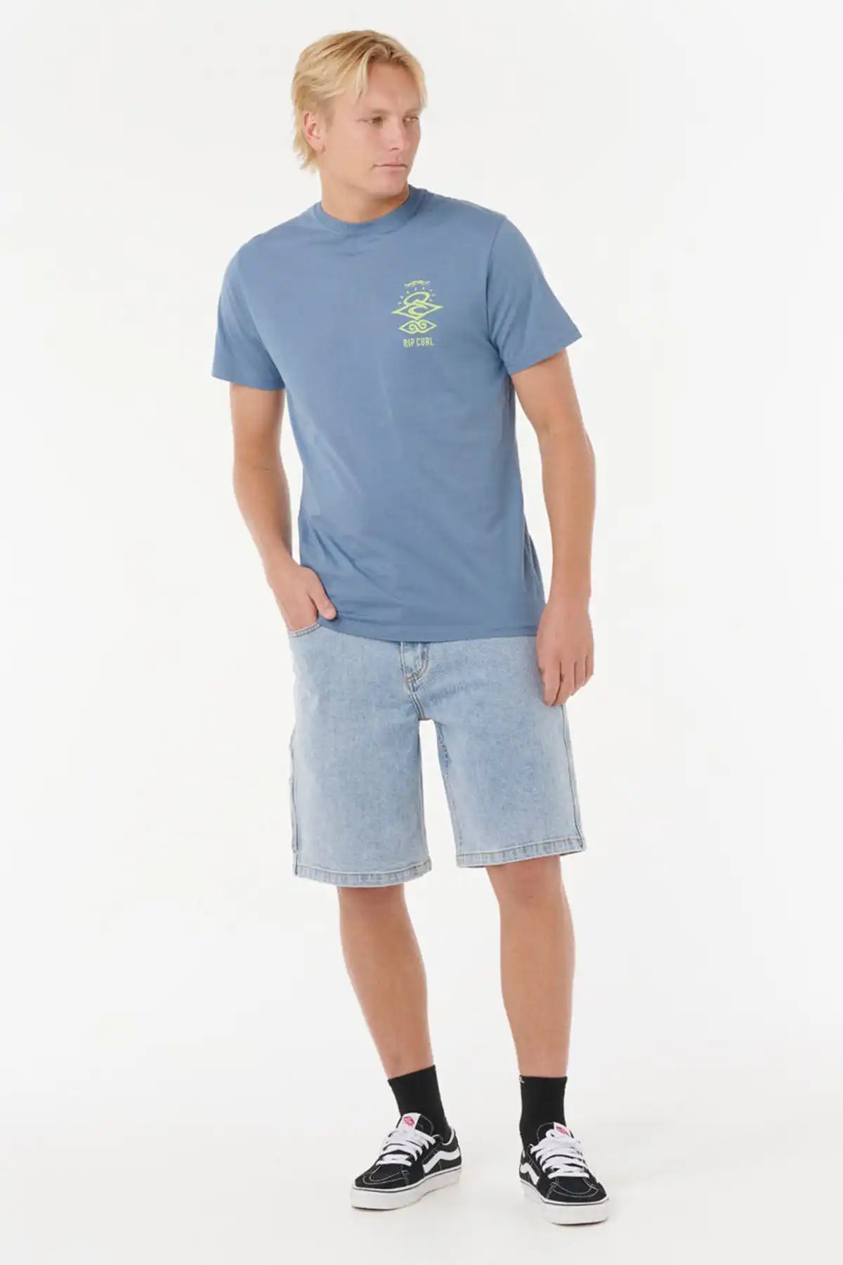 Man wearing a Rip Curl Mens Search Icon Tee in Blue Fin with a logo and light blue shorts on a white background full model view