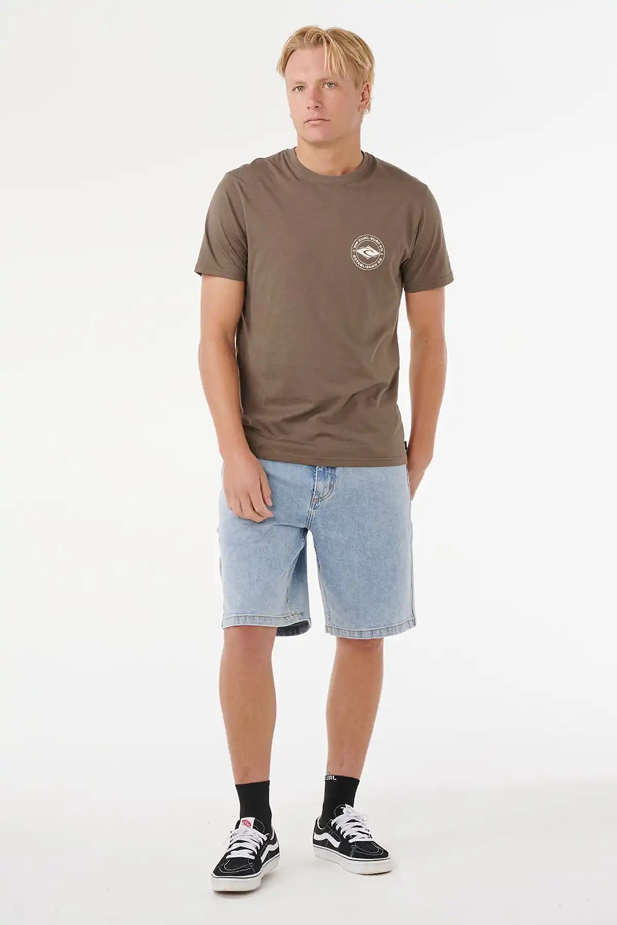 Man wearing a brown t-shirt with a logo and light blue shorts on a white background