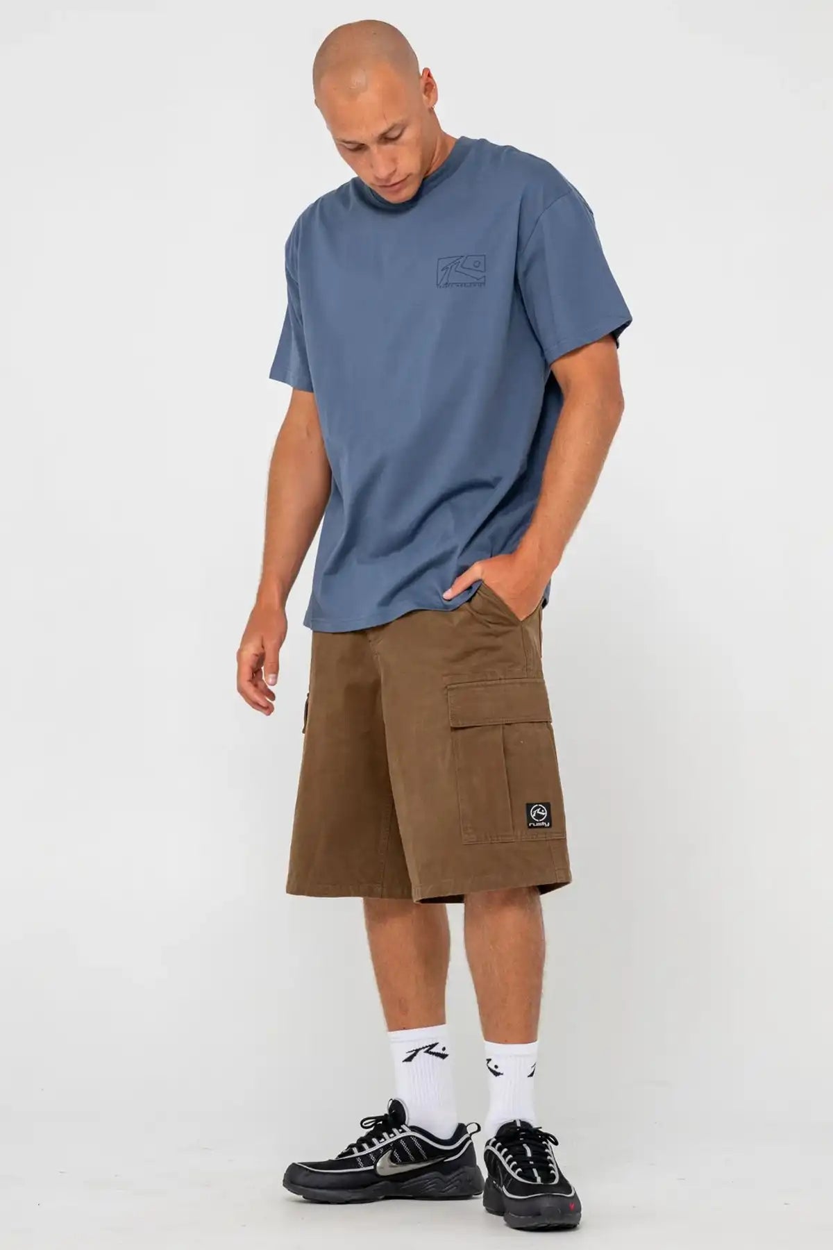 man wearing a Rusty Boxed Out Graphic Tee in China Blue with small rusty logo on chest and pinecone shorts on a white background