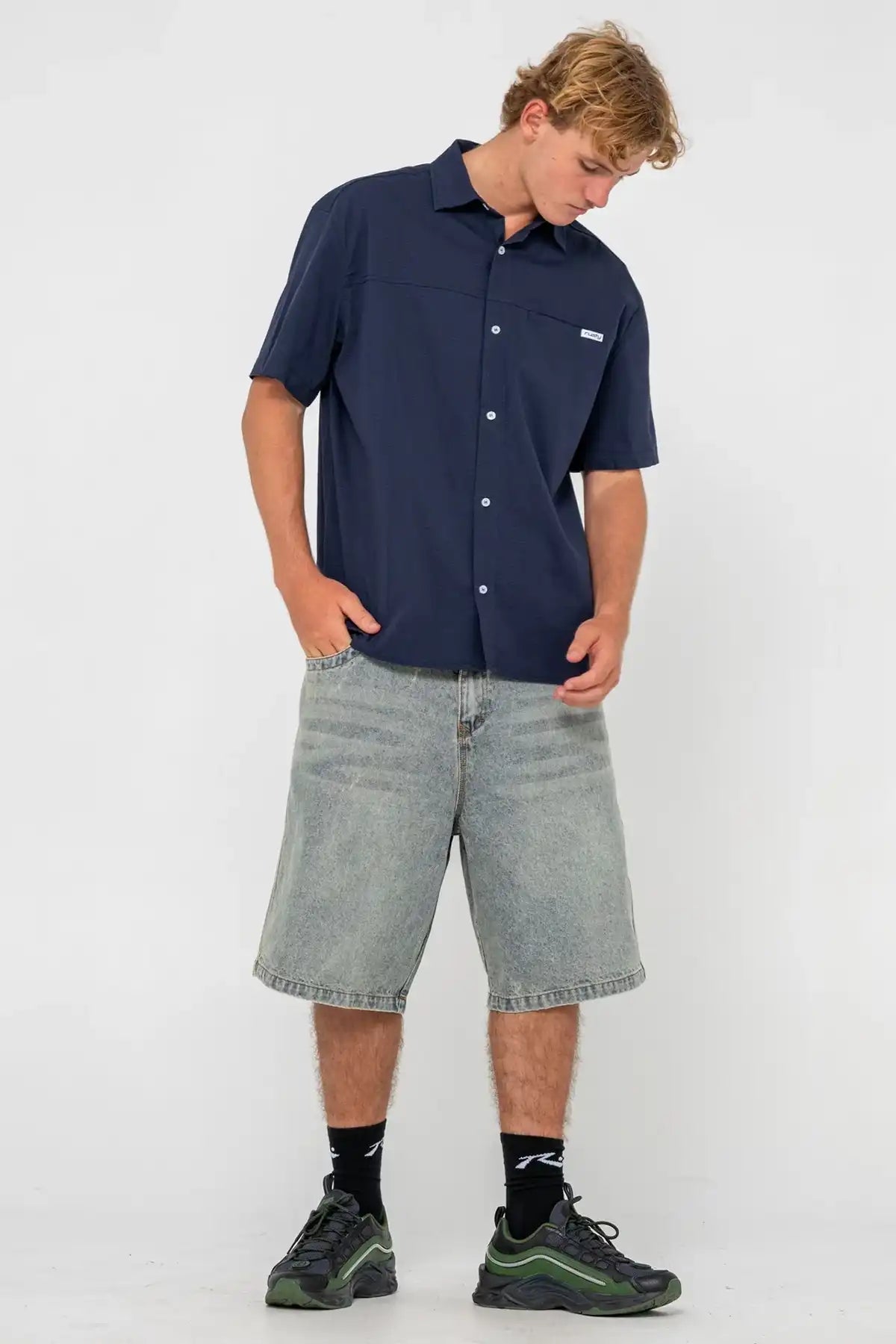 man wearing Navy Blue Rusty Giles Short Sleeve Shirt and denim shorts against a white background