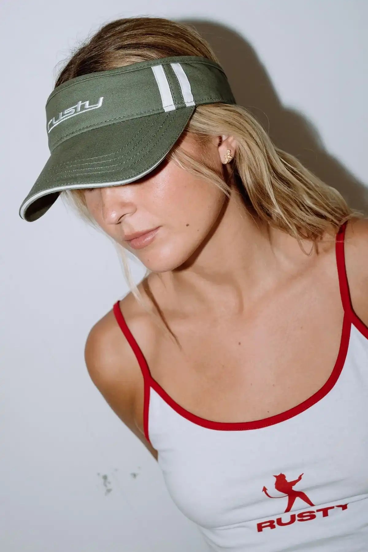 Woman wearing a Rusty Love Visor in Arm Green and white tank top with red accents, featuring the Rusty brand.
