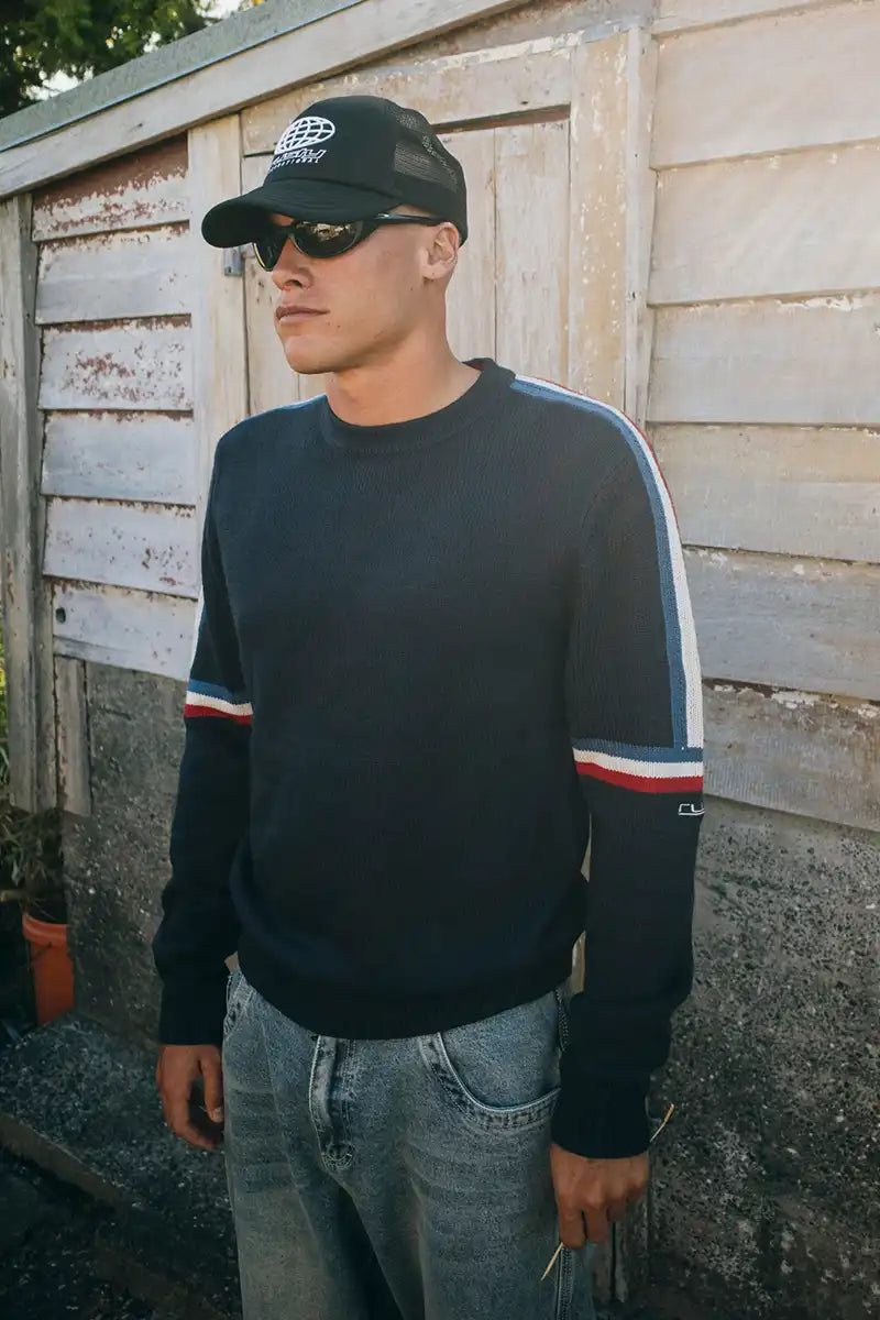 Rusty Mens Moritz Crew Knit in Navy Blue feature image near an old shed