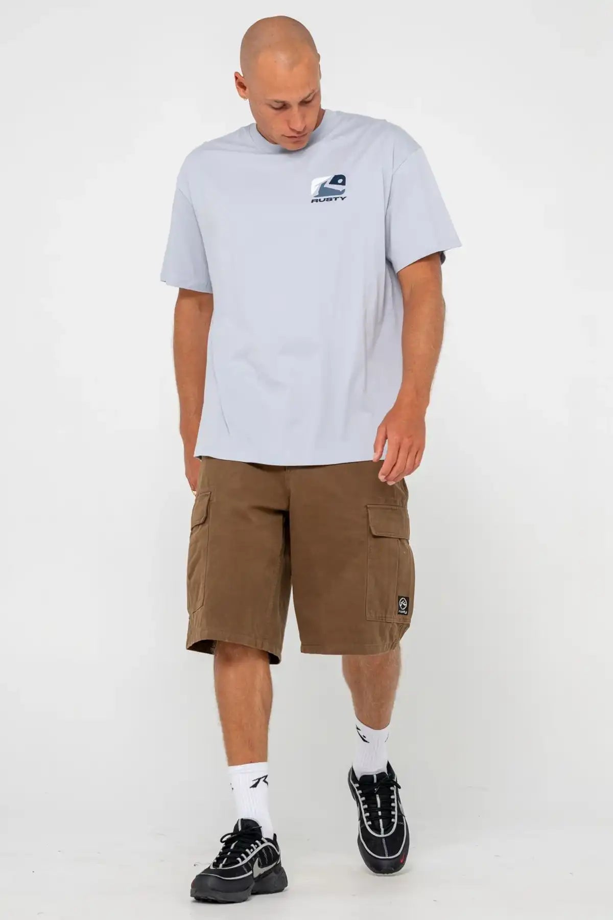 Man wearing Rusty Mens Phenom Graphic Tee in Smoke Blue and pinecone shorts on a white background