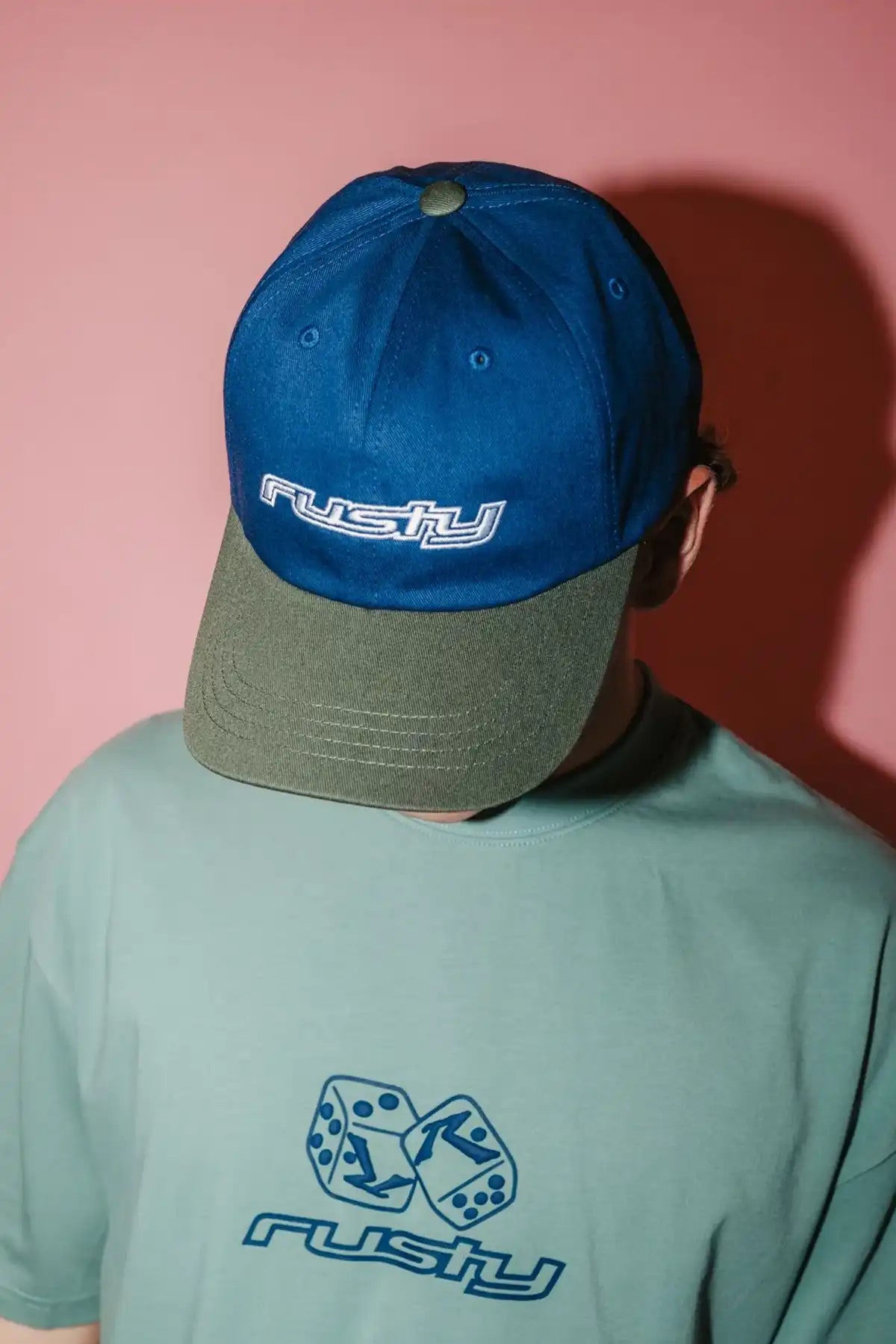 Person wearing a Rusty Rusty Road Trip Dad Cap in Navy Blue with 'Rusty' branding against a pink background