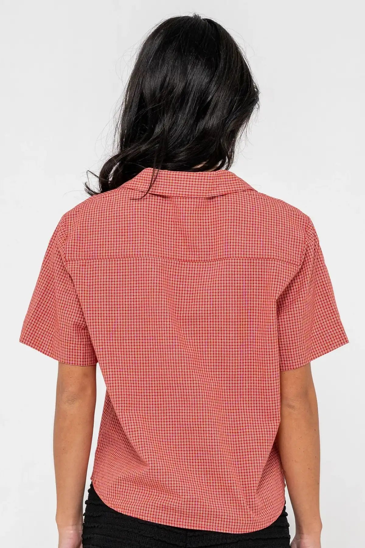 woman wearing Rusty Summer Court red Boxy Shirt and black shorts on a pink background back on view