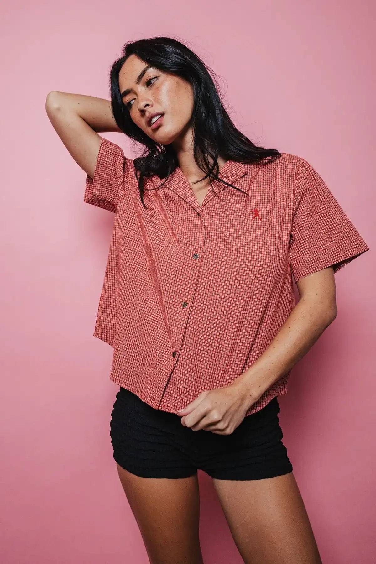 woman wearing Rusty Summer Court red Boxy Shirt and black shorts on a pink background