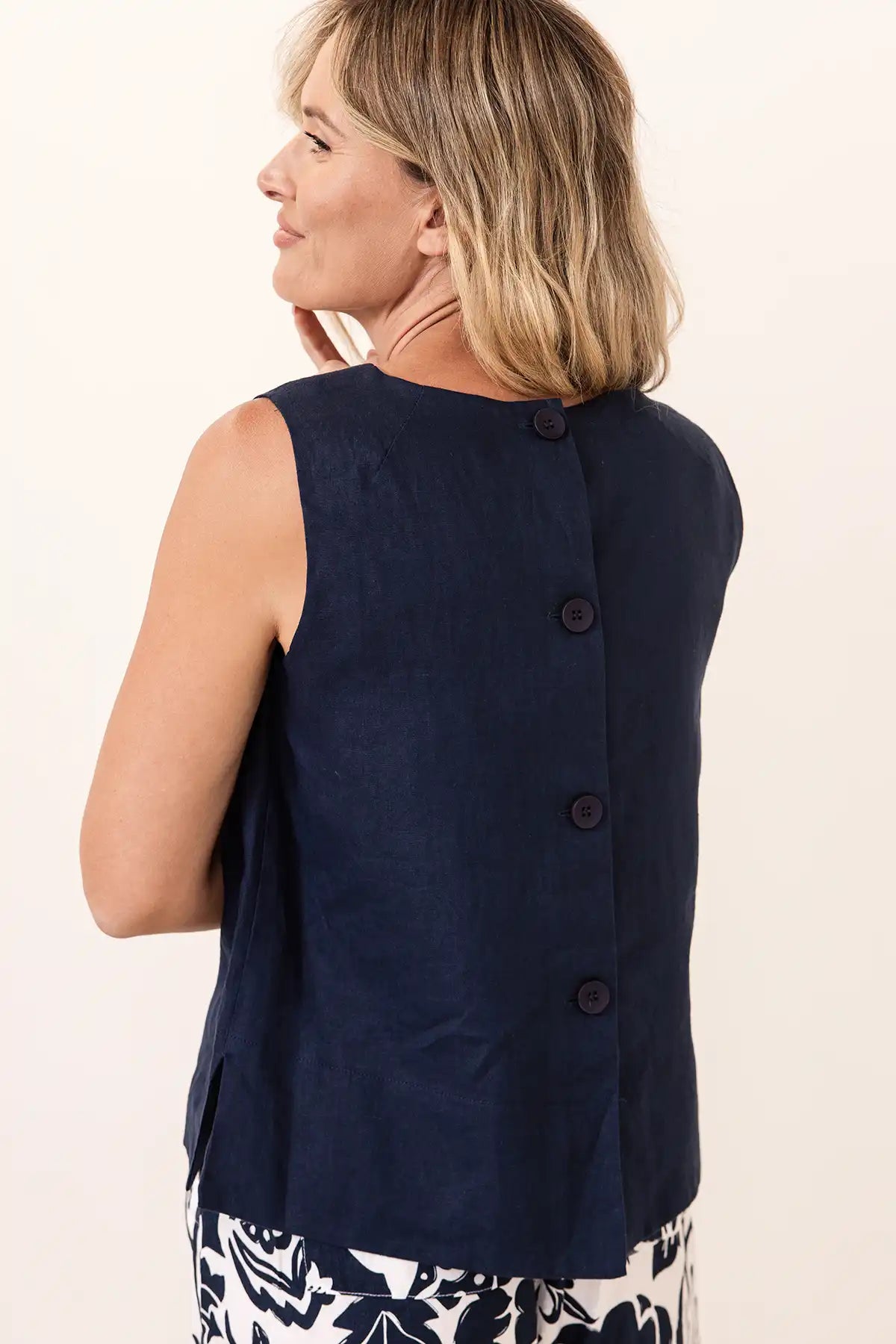 Woman wearing a navy sleeveless top with buttons on a light background