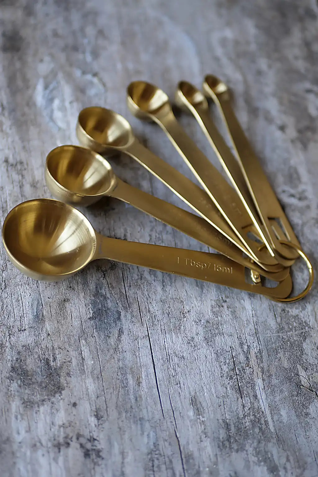 Brass coloured measuring spoons on a piece of weathered timber