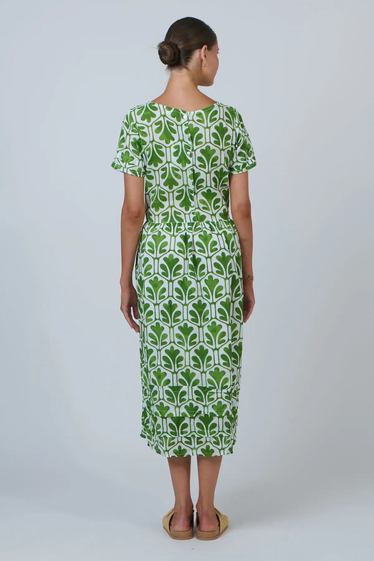 back on view of lady wearing a white and green dress with leaf print on a white background