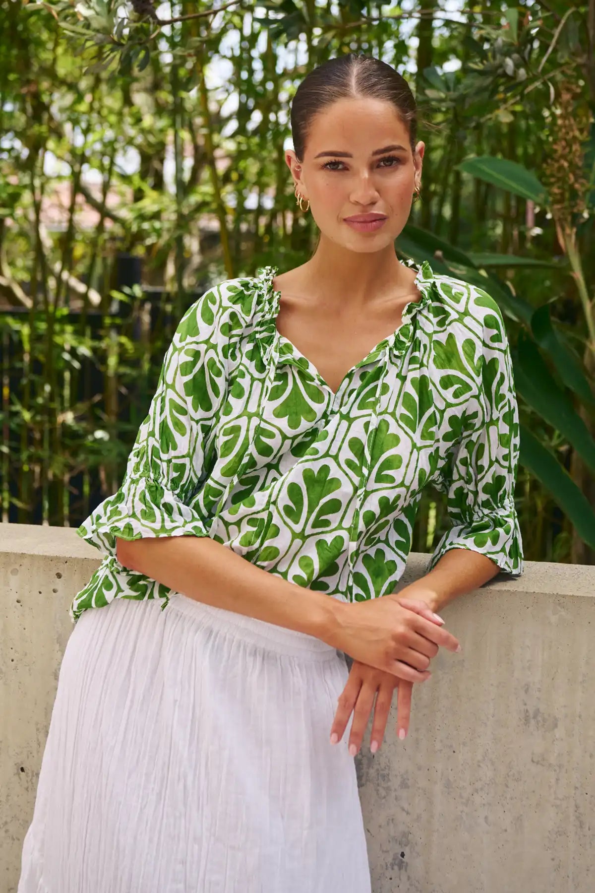 woman wearing the Summer Garden Crinkle Cotton Top and white skirt in the garden leaning against concrete wall
