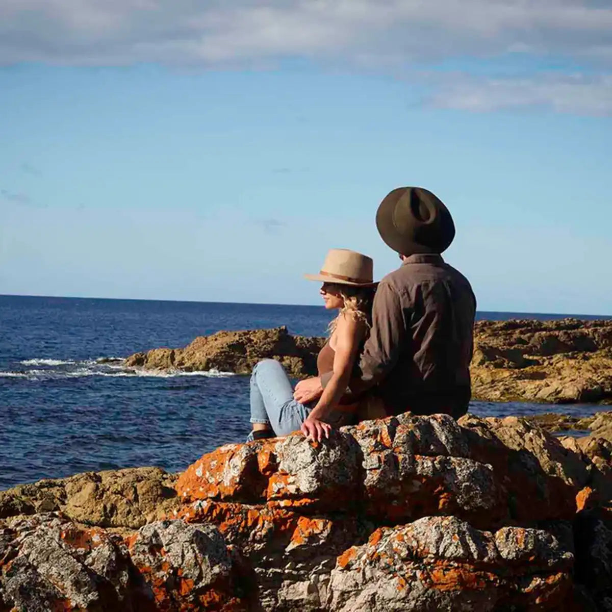 Couple sitting on rocks of the Tasmanian Coast overlooking the ocean