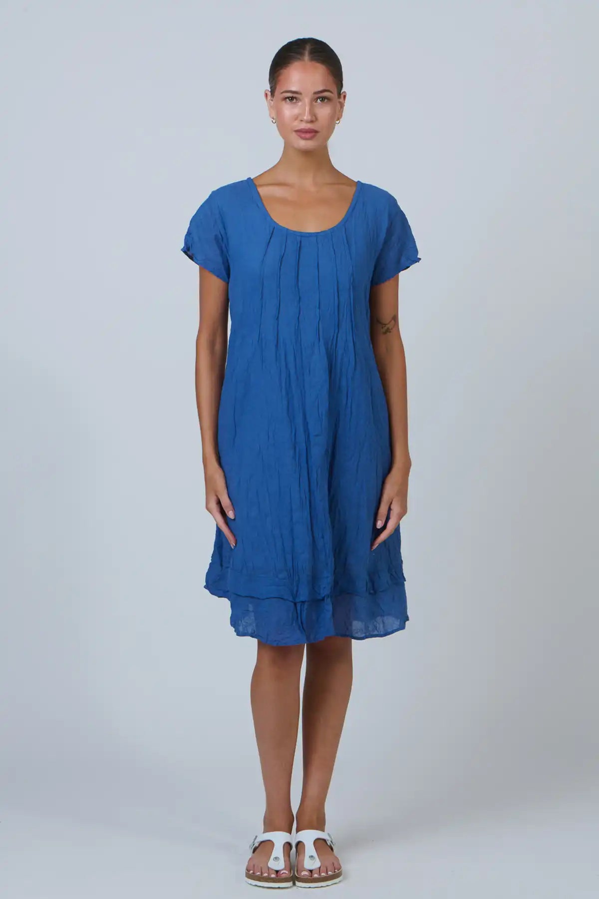 woman wearing the Tidal Pleat Cotton Dress in Ocean Blue against a white background with hands by her side