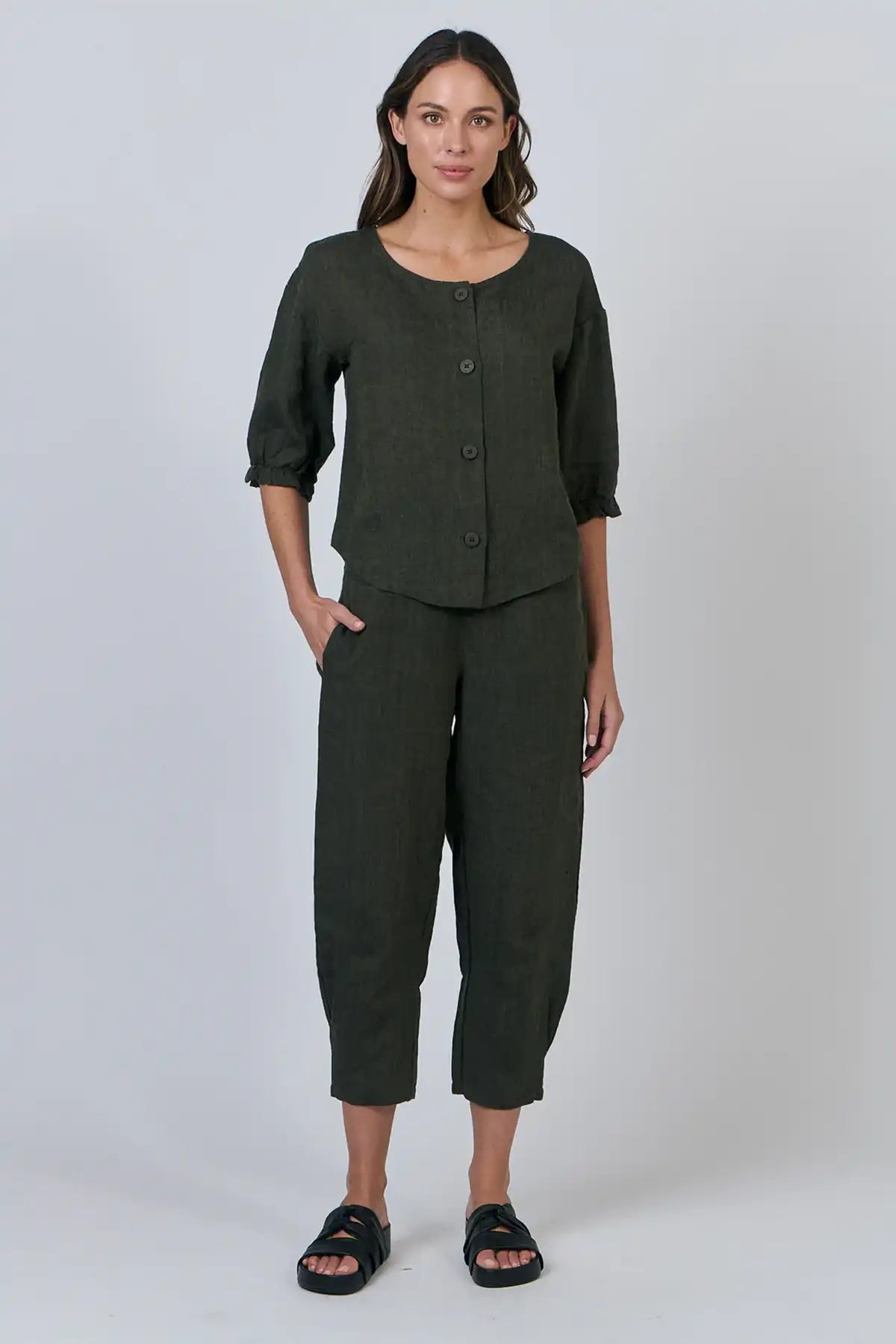 Woman wearing a dark green outfit with a buttoned top and wide-leg pants on a white background