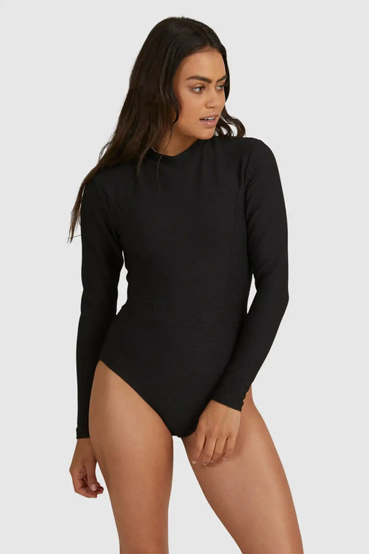 Woman wearing a Billabong Tanlines Bodysuit Rash Vest in Black long-sleeve bodysuit on a white background