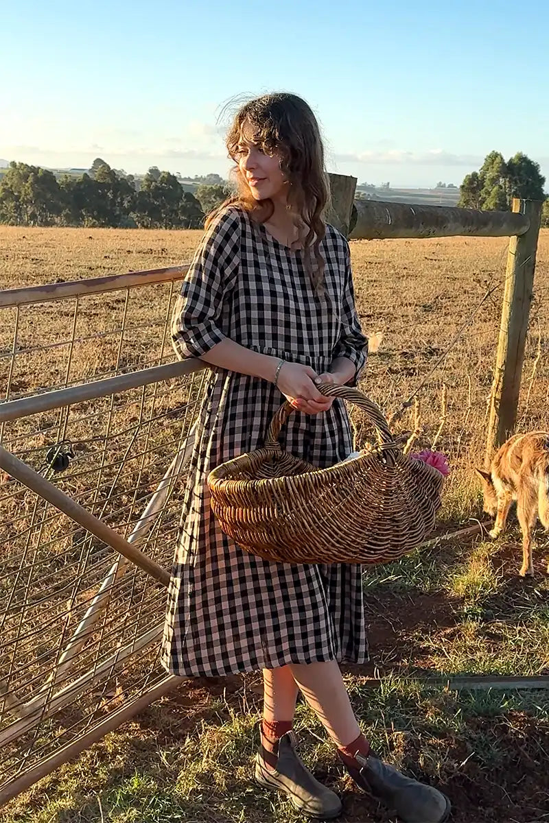 Black Gingham dress 3/4 view with model leaning on the farm gate