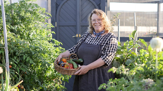 Rachille standing in the garden wiht a basekt full of freshly picked produce. Wearing the Sofia Pinafore dress and neckerchief
