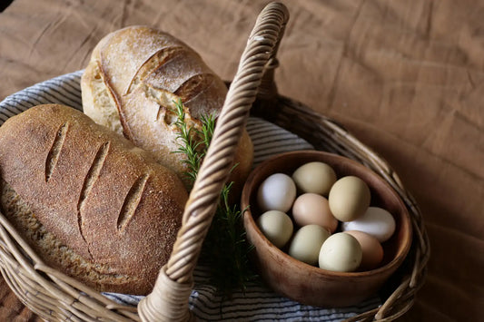 a white loaf of sourdough and a wholewheat loaf of sourdough and some eggs in a basket